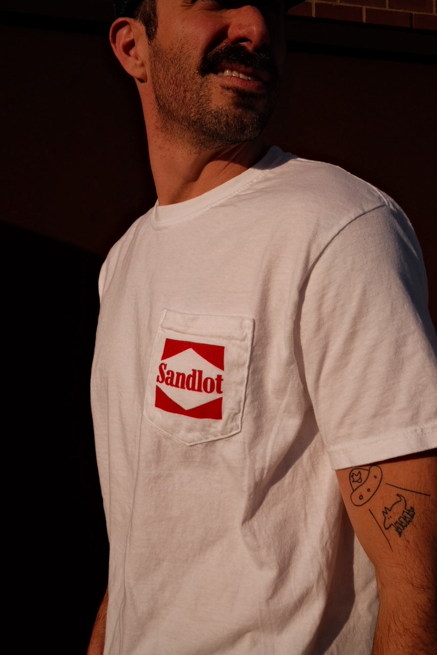 Close-up of Sandlot logo in red on the front pocket of a white tee.