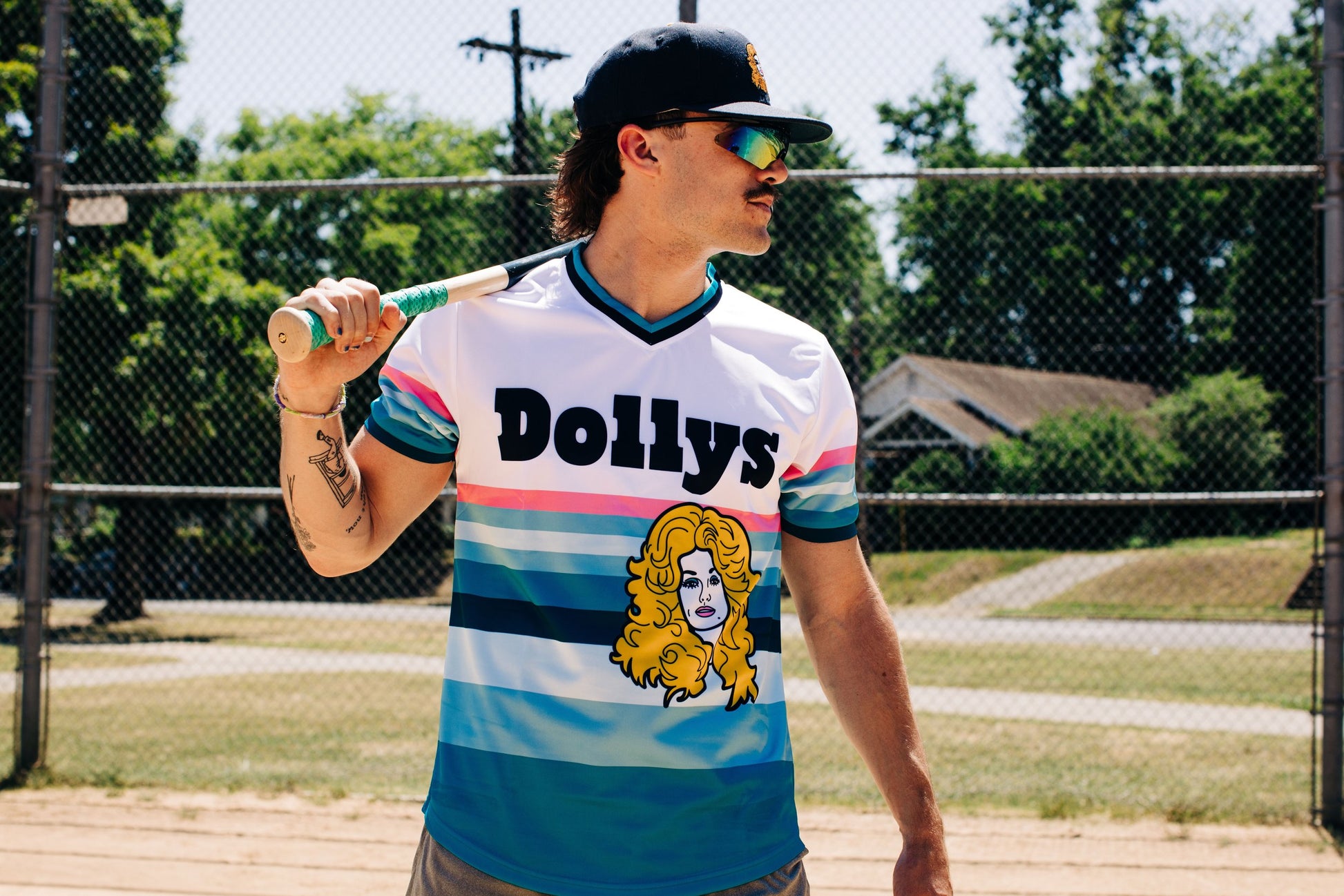 Person in Retro 'Sunset' Jersey with Dolly Parton logo holding a bat on a baseball field.