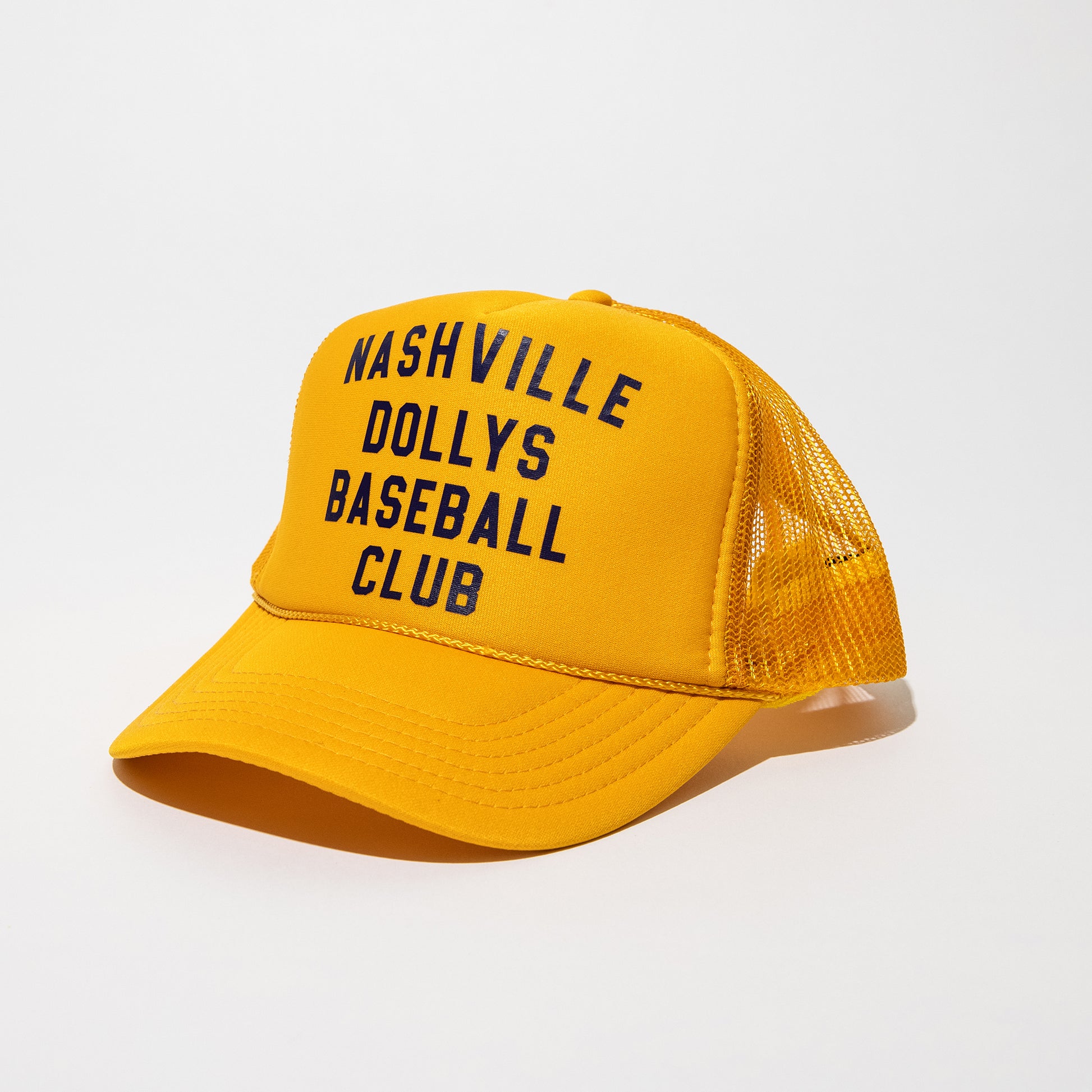 Angled side view of a yellow Nashville Dollys Baseball Club retro trucker hat with black text.