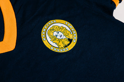 Close-up of Dolly Parton’s face logo on a navy tee with yellow trim.